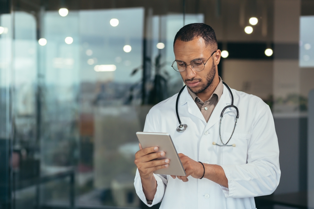 Médico de jaleco e estetoscópio consultando um tablet